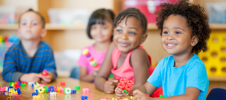 Four young children sit around a table with colorful toys